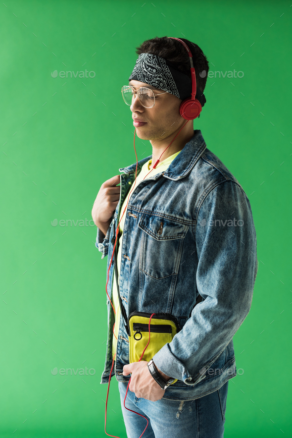 handsome mixed race man in headphones and denim listening music on green screen