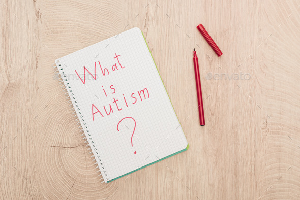 top view of red opened marker and what is autism question written in notebook on wooden table