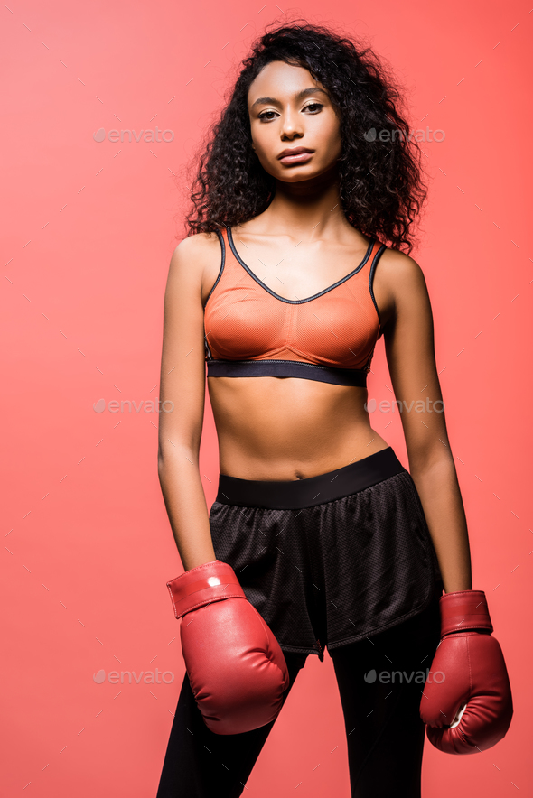 beautiful african american sportswoman in boxing gloves looking at camera and posing isolated on