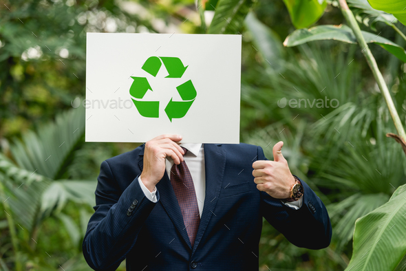 businessman holding white card with green recycling sign in front of face and showing thumb up in