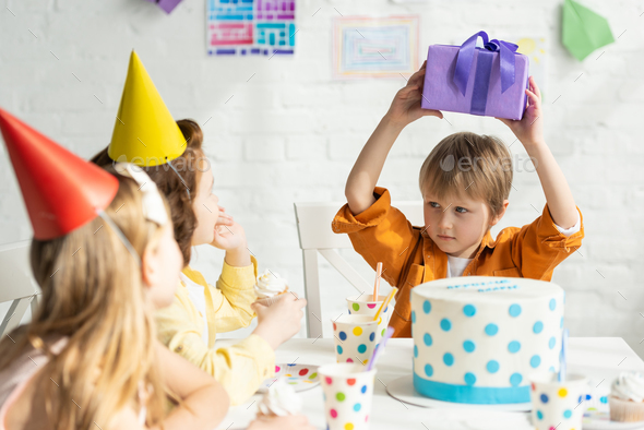 boy holding present while sitting at table with friends during birthday ...