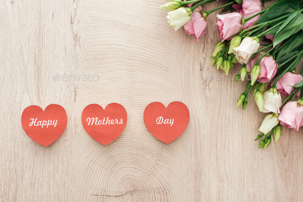 top view of heart-shaped cards with happy mothers day writing and eustoma flowers on wooden table