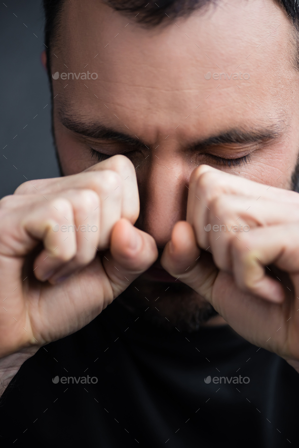 depressed crying man with closed eyes wiping tears away with hands