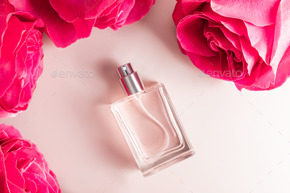 A transparent bottle of women s perfume or eau de toilette lies among the large buds of pink roses