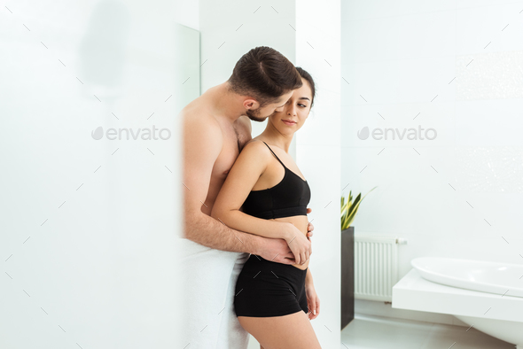 attractive and smiling girlfriend in black underwear sitting on boyfriend  in bed Stock Photo by LightFieldStudios