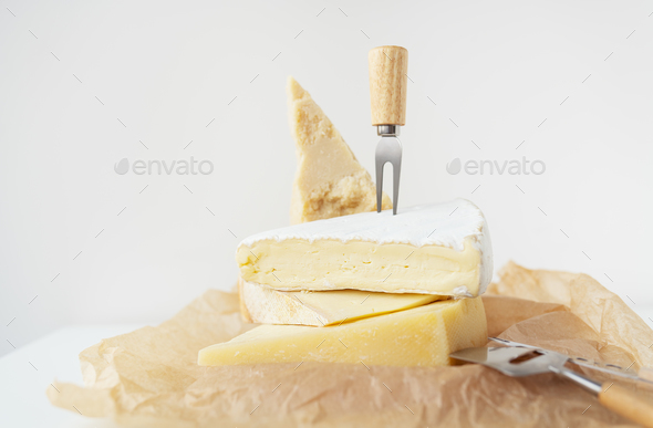 Different types of cheese lie on top of each other with cheese knives on parchment. A delicacy.