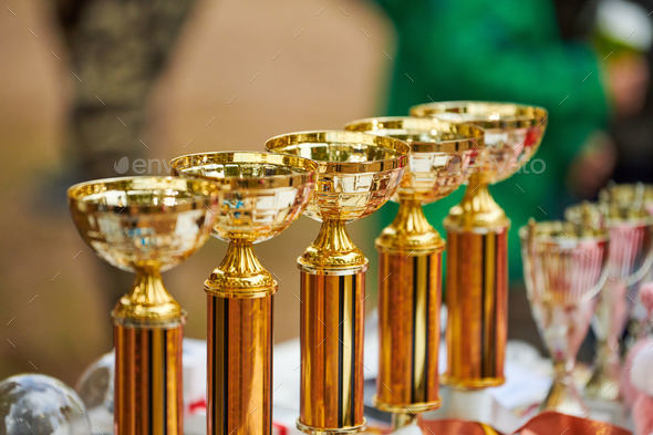 Champion golden trophies, many shiny golden trophy cups lined up in row on table, trophy awards