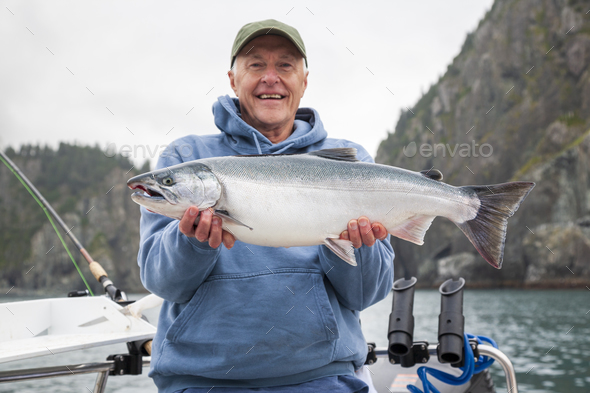 Selective focus view of a happy senior fisherman holding up a nice silver salmon in Alaska - Stock Photo - Images