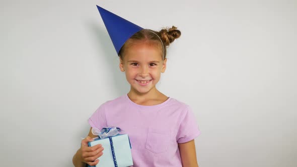 Portrait of a Girl Wearing Birthday Cap and Holding Noise Maker. Funny Young Girl Comes and Whistles alt