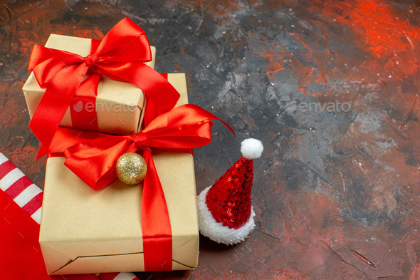 bottom view small gifts tied with red ribbon santa hat on dark red table  free space Stock Photo by ImgSolut