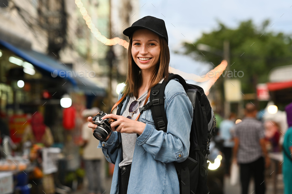 Portrait of hipster female tourist with digital camera standing in night market
