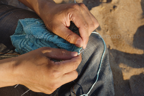 palms of men knits blue yarn openwork pattern with metal knittings on beach on sunny day