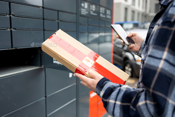 A man with a box in his hands near the self-service mail terminal. Parcel delivery machine. Person h