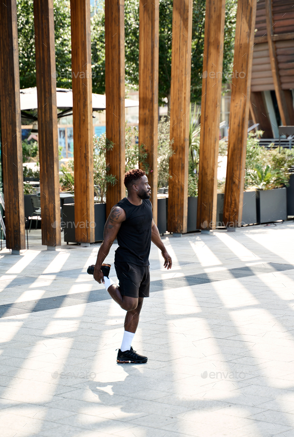 Fit sporty young black man doing warm up exercises in workout park