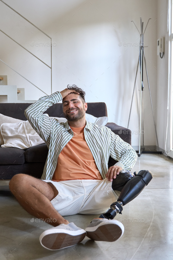 Happy relaxed amputee man with leg prosthesis sitting on floor at home.