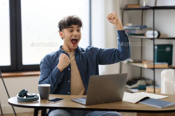 Joyful Arabic Man Looking At Laptop Shaking Fists In Office