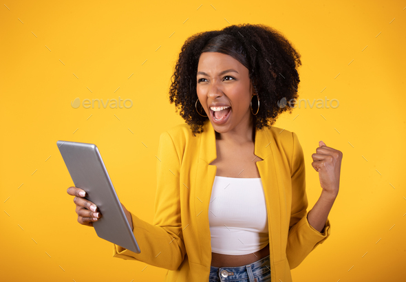 Yes. Excited black lady celebrating success with digital tablet, raising clenched fist and