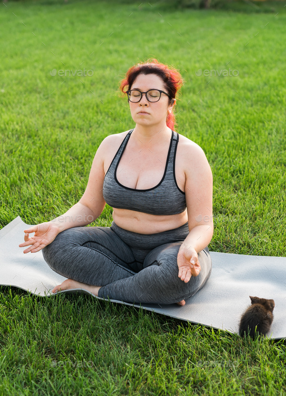 Plus size body positivity woman doing meditation on yoga mat with kitten on  backyard - wellness and Stock Photo by Satura_