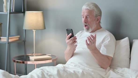 Failure Old Man Reacting to Loss on Smartphone in Bed alt