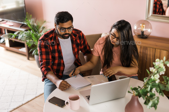 Young millennial indian husband and wife doing domestic paperwork, accounting job and reviewing
