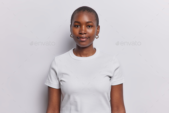 Portrait of serious dark skinned woman with neutral facial expression looks directly at camera