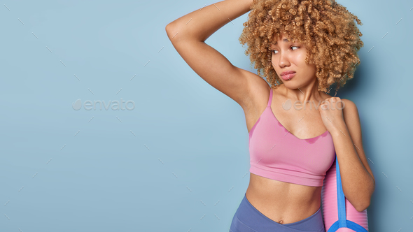 Slim sportswoman raises arm frowns face because on unpleasant smell being sweaty after hard training