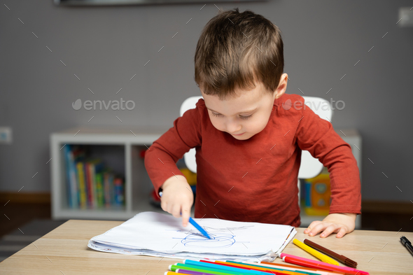 A cute little toddler boy of two years old draws with markers in the album in the children's room  - Stock Photo - Images