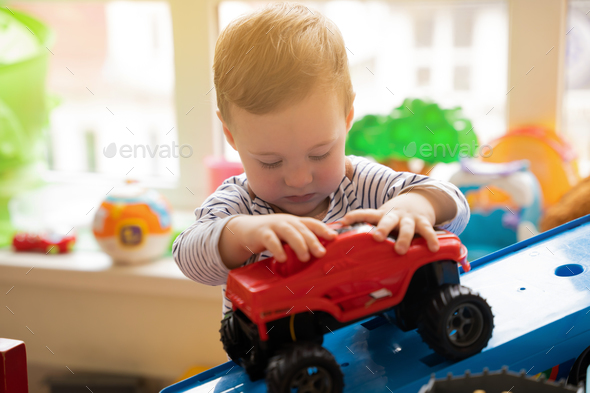 Toddler boy plays with car toys in the children's room. E - Stock Photo - Images