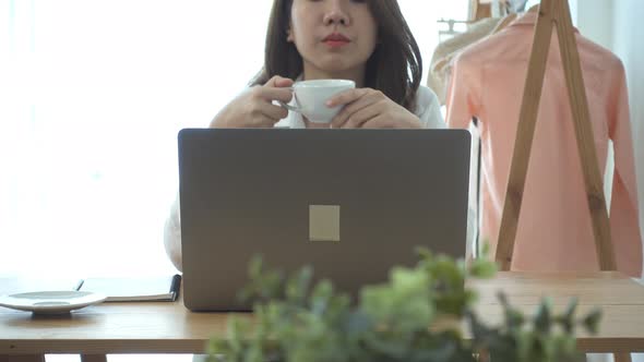 young smiling woman working on laptop while enjoying drinking warm coffee sitting. alt