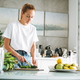 Young woman in white t-shirt and blue jeans cooking healthy food with cucumber in kitchen at home - PhotoDune Item for Sale