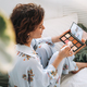 Young woman in blue pajamas applies makeup with face sculpting palette sitting on bed at home - PhotoDune Item for Sale
