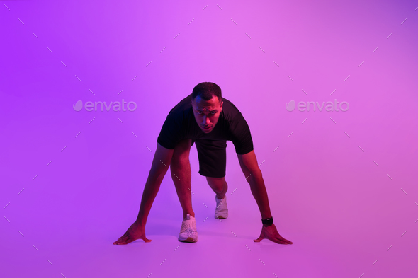 African Sportsman Posing In Crouch Start Position On Purple Background