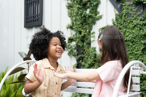 Happy two kid little girls sitting on bench enjoy playing hand clapping game in outdoor at home.