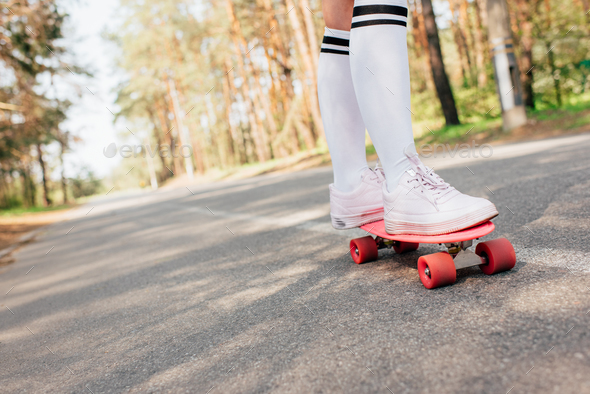 partial view of girl in knee socks skateboarding on road