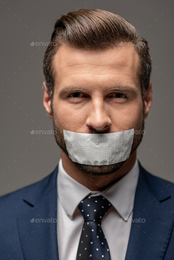 handsome businessman in suit with duct tape on mouth isolated on grey