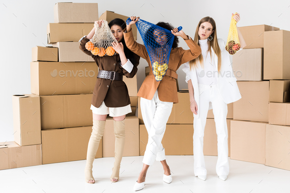 african american girls covering faces while holding string bags with fruits near blonde woman on
