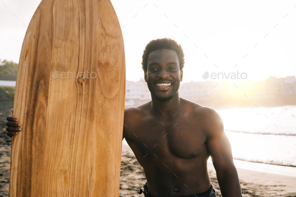 Happy African surfer holding surf wood surfboard after riding waves on the beach - summer vacation
