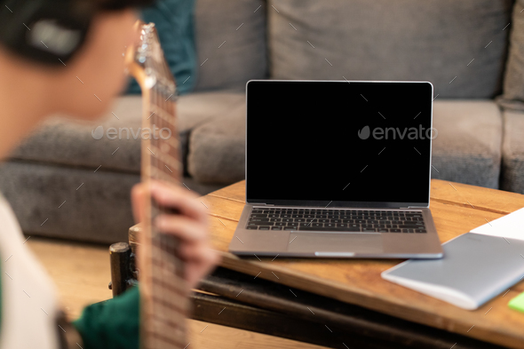 Guy Playing Electric Guitar Near Laptop With Blank Screen Indoors