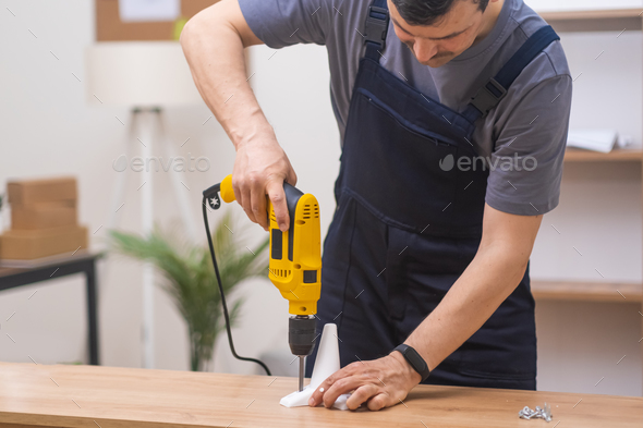 Furniture manufacturing and delivery handyman in uniform attaching legs to rack with screwdriver