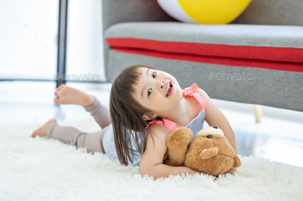 Cute smiling down syndrome girl in living room with teddy bear.