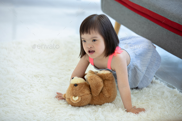 Cute smiling down syndrome girl in living room with teddy bear.