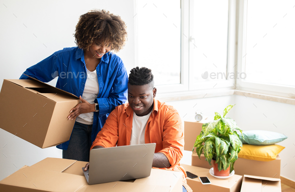 Cheerful Black Couple Using Laptop, Checking Moving Companies Online While Relocating Home