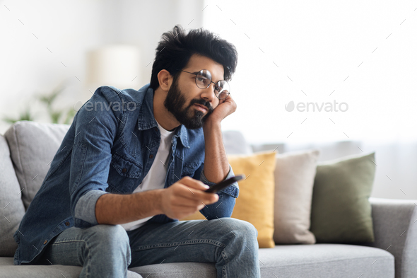 Boring Show. Portrait Of Upset Young Indian Guy Watching TV At Home,