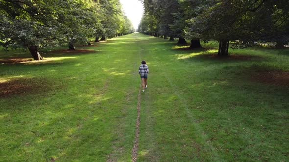 Woman walking away in the park with grass and trees on sunset Aerial