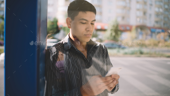 Asian guy using smartphone on bus stop in city