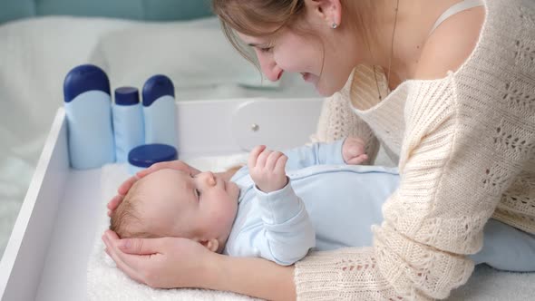 Smiling Mother Stroking and Smiling at Her Little Baby Boy Lying on Dressing Table at Bedroom alt