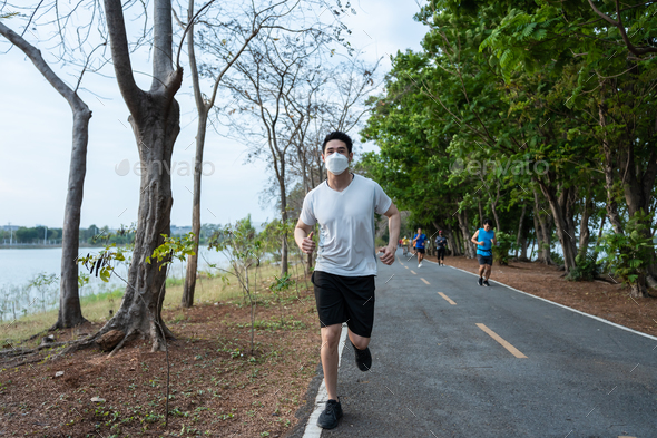 Asian young active sport man wearing mask run on street in public park.