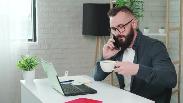 Handsome Bearded Man Drinking Coffee While Talking on a Smart Phone alt