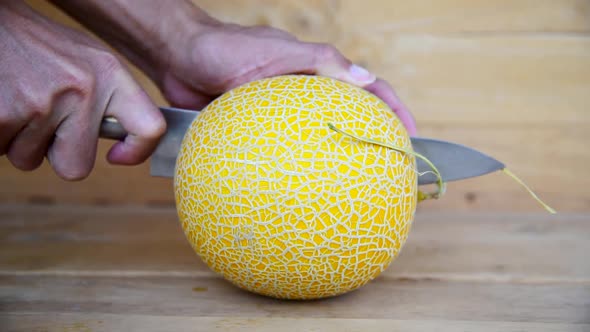 The man use knife split the yellow melon on wood plate alt