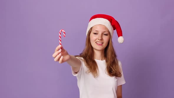 Woman White Tshirt Red Santa Claus Hat Holds Sweet Lollipop Licks Her Lips alt